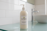 16 oz clear plastic bottle with white plastic pump with Coffee Oat white lotion, jar has label with Lux Natures with logo with small green leaf. Jar stands on the clear glass top in the clean modern bathroom on the background.