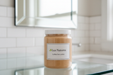 16 oz clear plastic jar with white plastic lid with Coffee Oat lotion, jar has label with Lux Natures with logo with small green leaf. Jar stands on the clear glass top in the clean modern bathroom on the background.